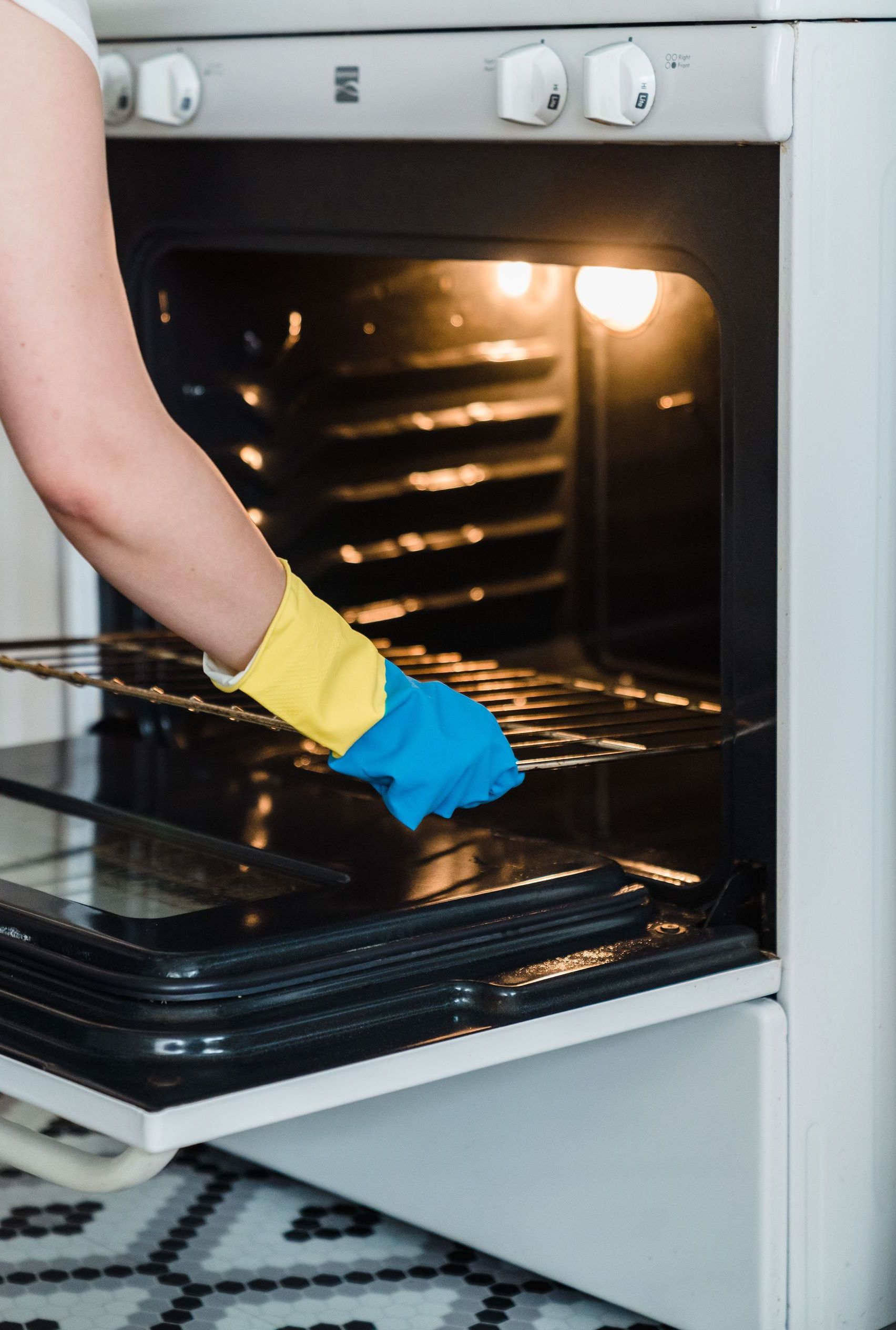 Adult woman cleaning an oven using protective rubber gloves indoors.